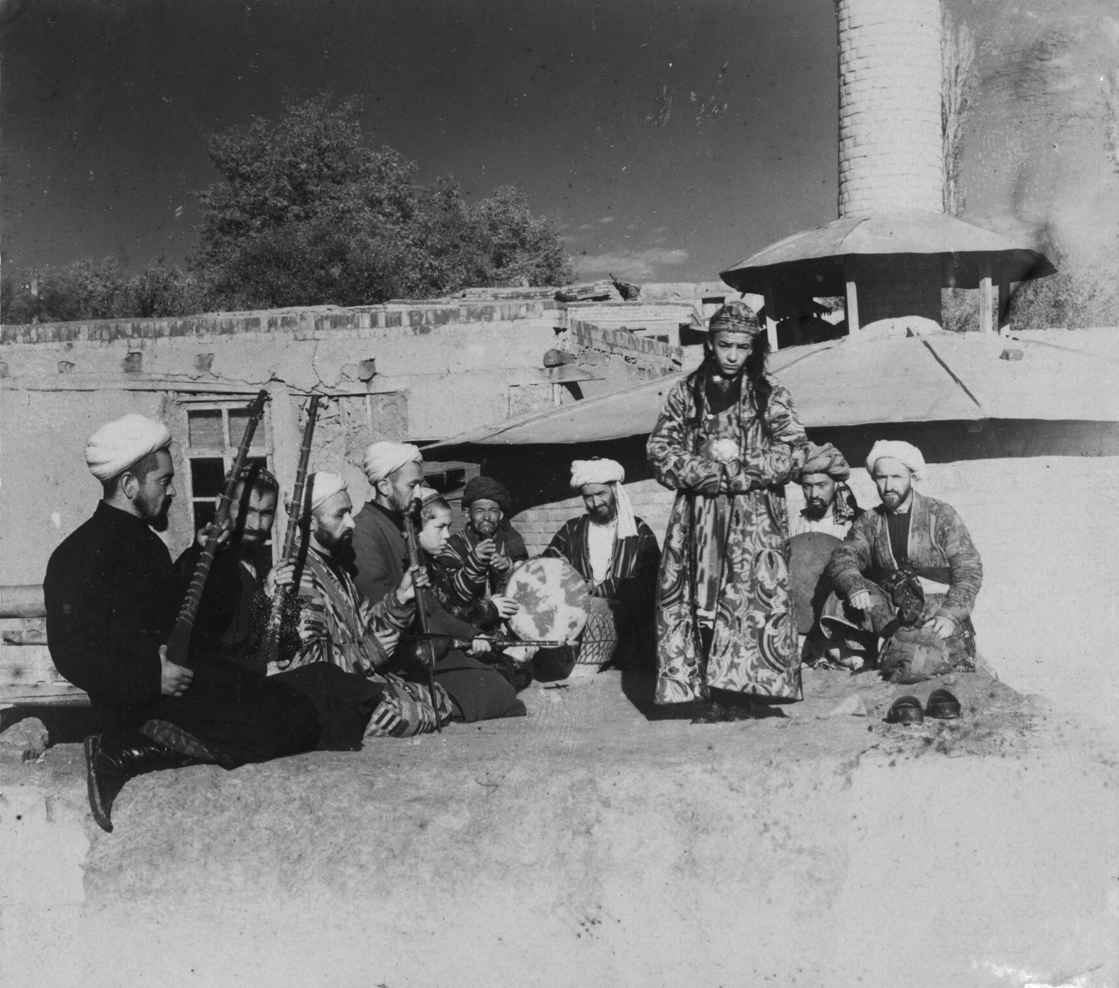 Historical nineteenth century photograph from Samarkand showing a group of traditional musicians playing instruments for a young bacha dancing boy.